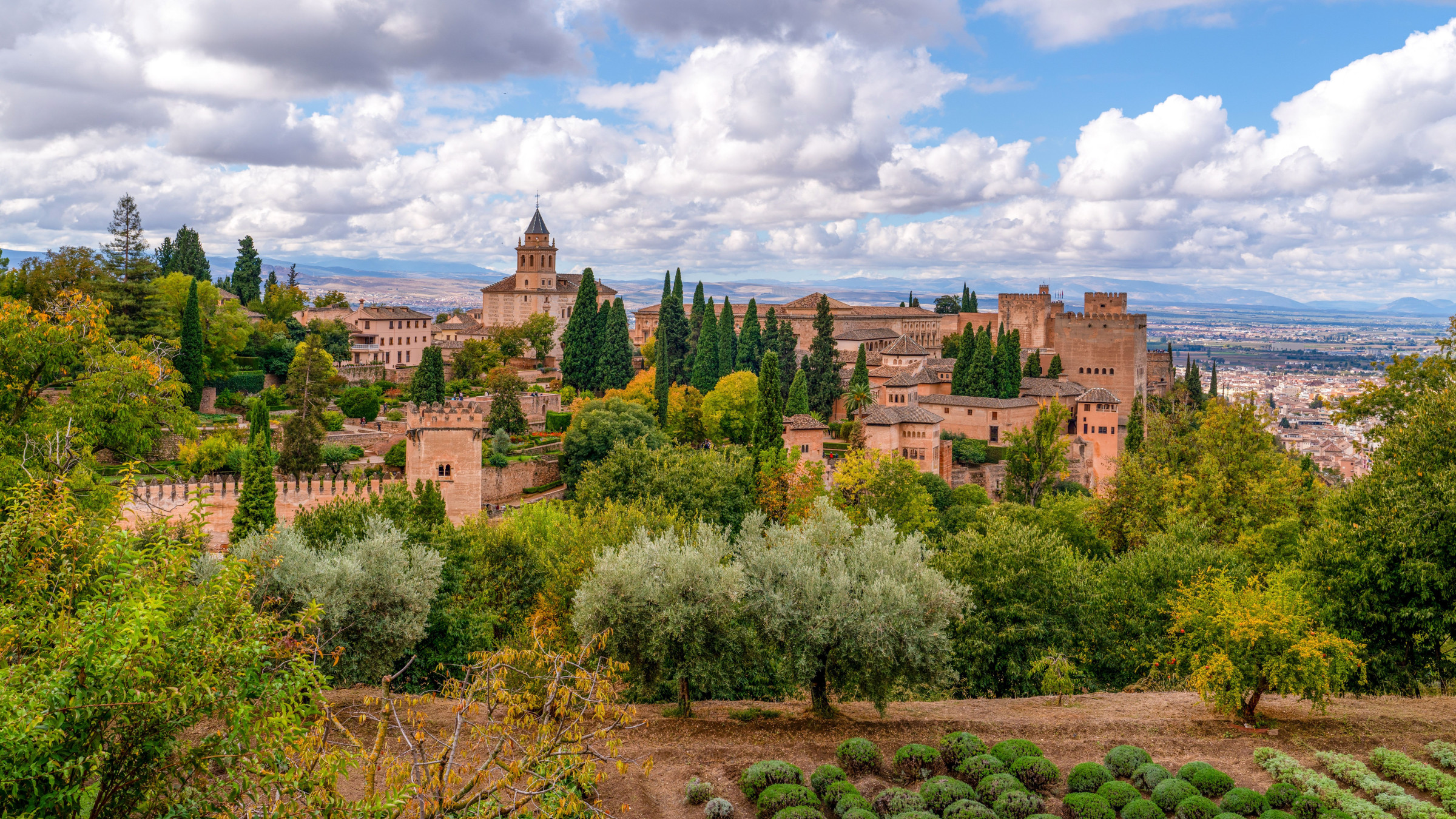 A panoramic view of the Alhambra complex amid countryside under a blue sky.