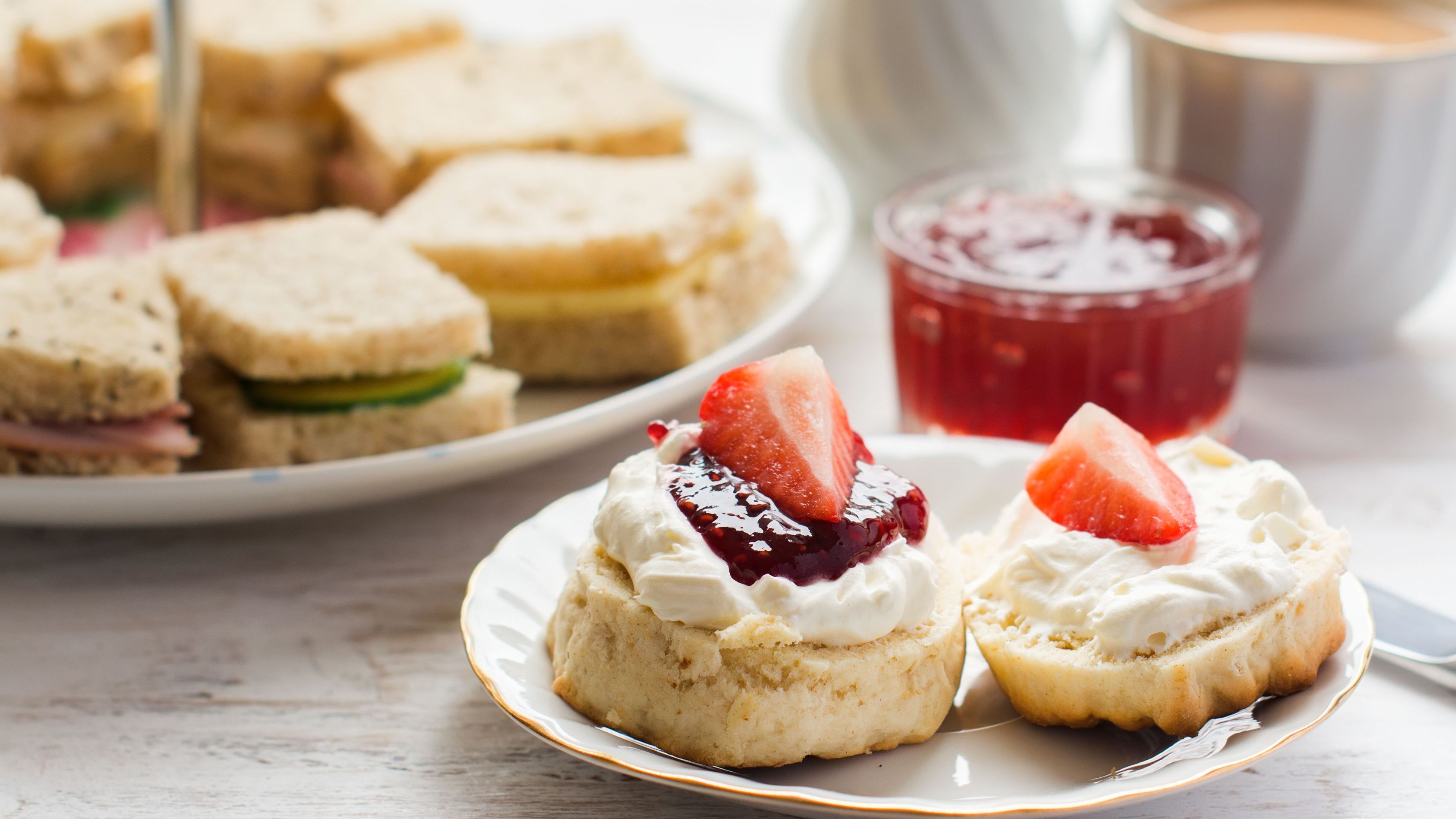 Traditional English afternoon tea: scones with clotted cream, jam, and strawberries, and various sandwiches on the background.