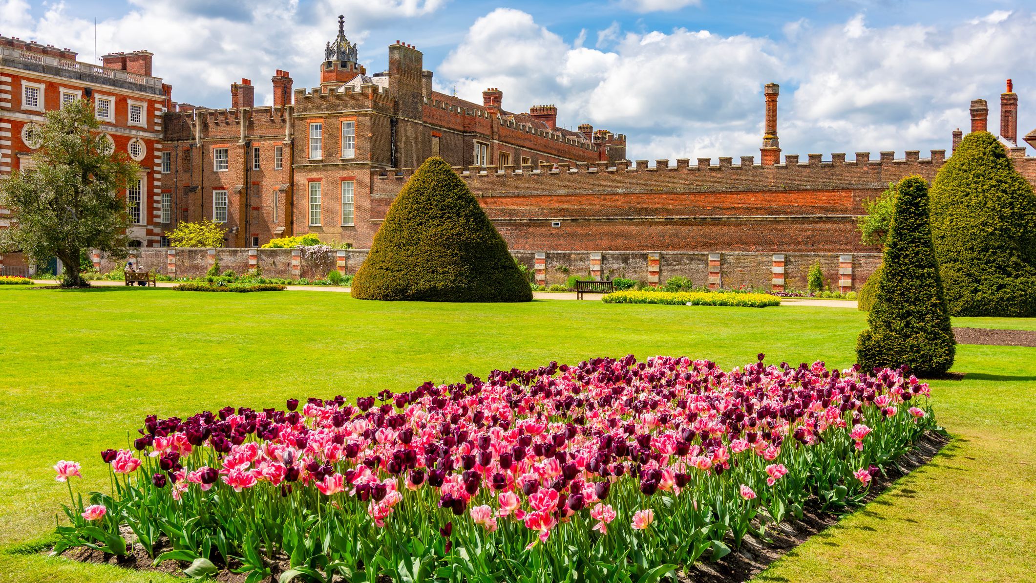 The Hampton Court gardens in spring. There's a brightly colored flower bed in the foreground.