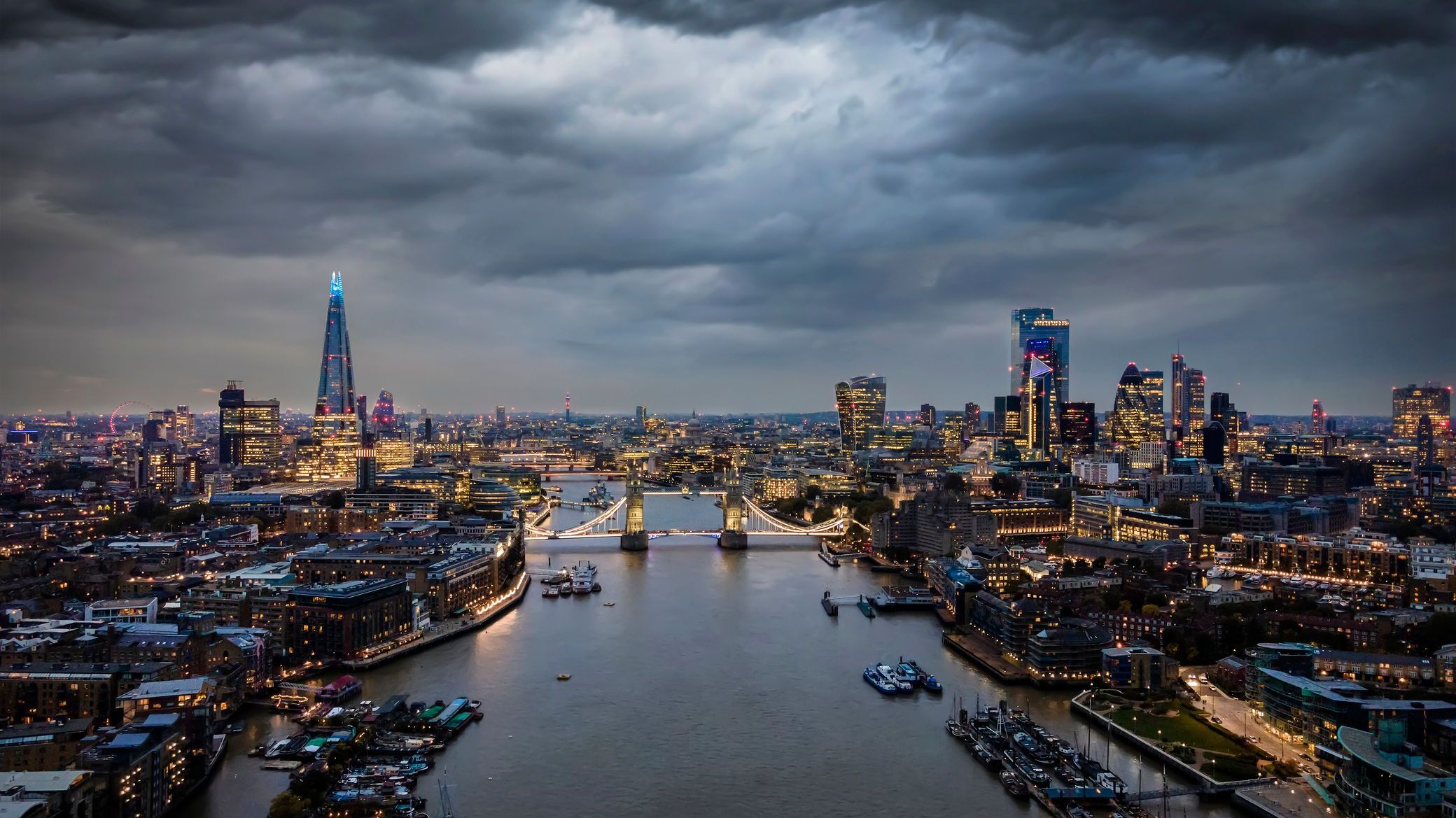 Elevated, moody view of the illuminated skyline of London, United Kingdom, with a cloudy sky at dusk.