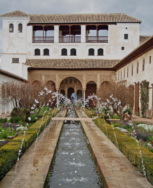 The Alhambra fortress in Granada, featuring red stone walls, Moorish arches, and hilltop views overlooking the city and mountains.
