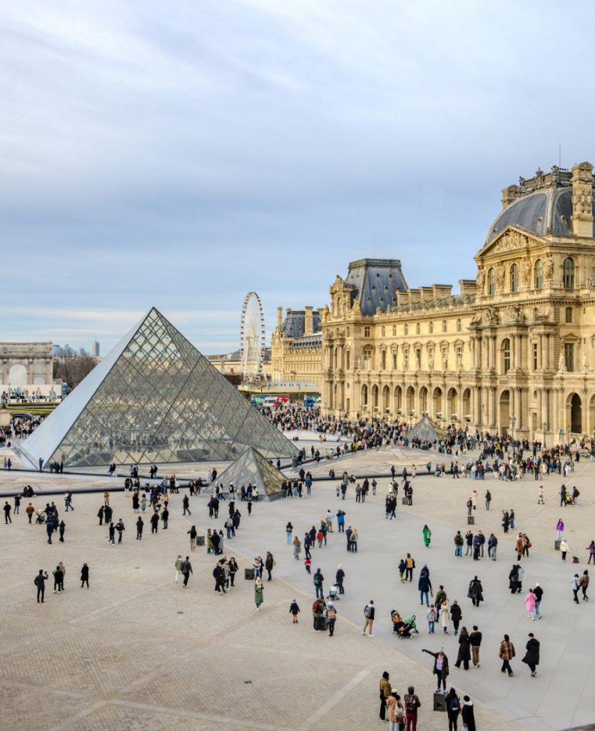 The Louvre Museum in Paris with its iconic glass pyramid in the central courtyard surrounded by historic architecture