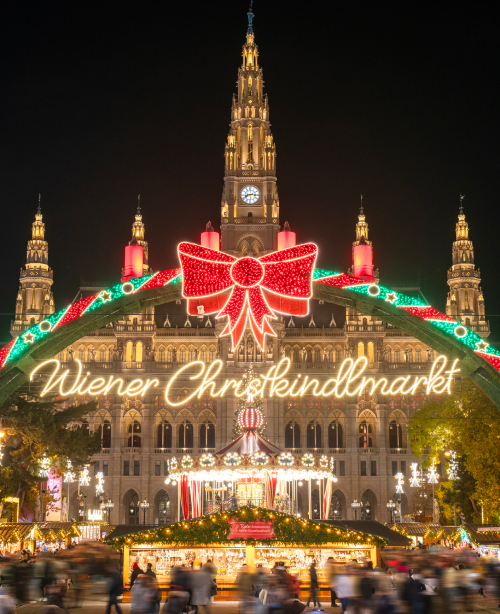 Christmas market in Vienna at night with glowing lights, festive stalls, decorated trees, and crowds enjoying the holiday atmosphere