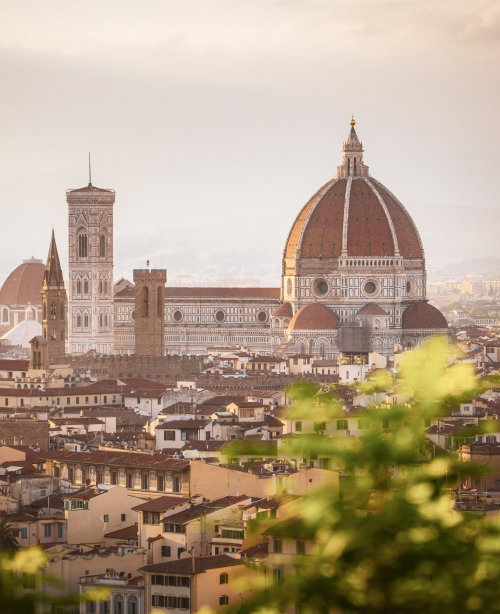 Panoramic view of Florence featuring the red-tiled Duomo dome, historic buildings, and the Arno River flowing through the city.