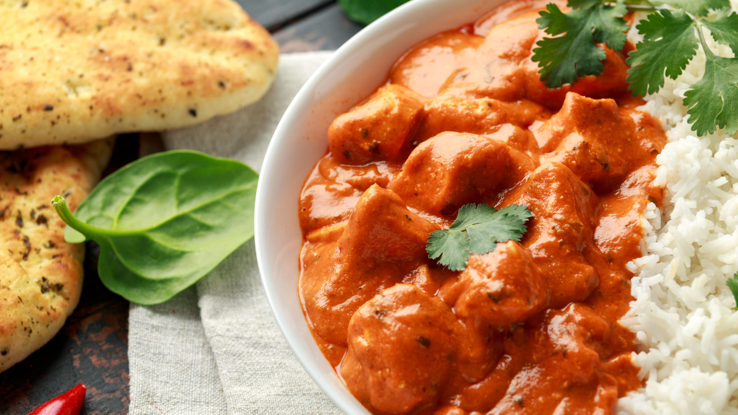 A close-up of chicken tikka masala served with white rice and naan bread. 