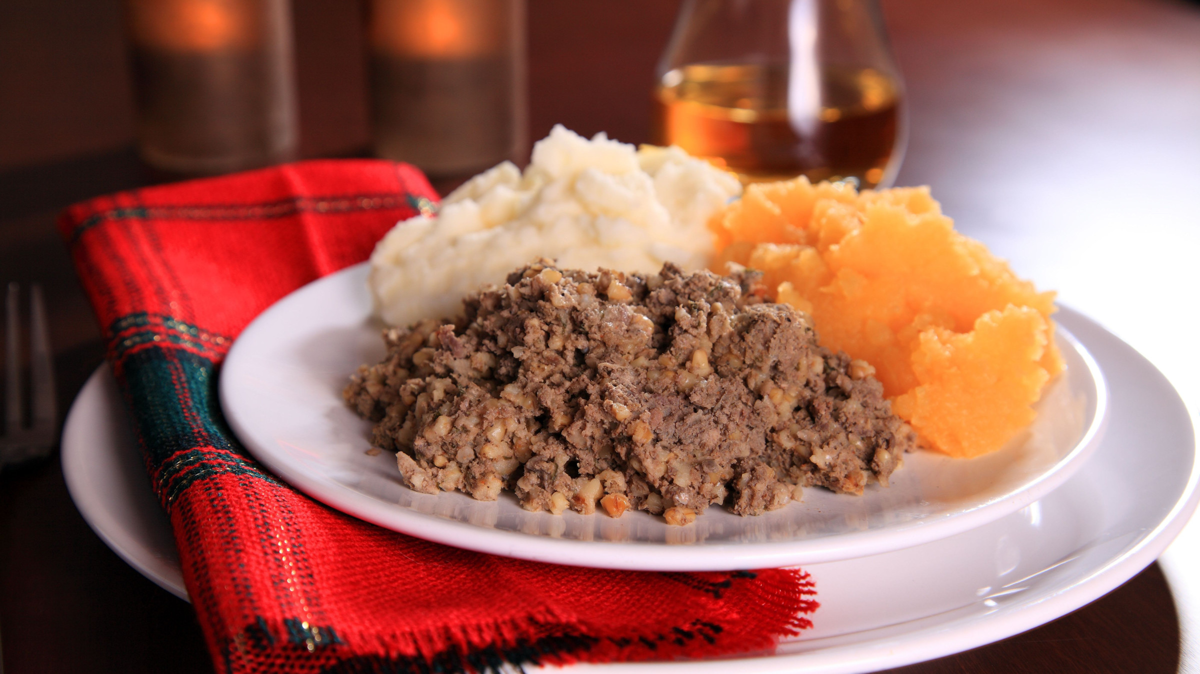 A white dish containing Haggis, Neeps & Tatties. There's a glass of whisky in the background. 
