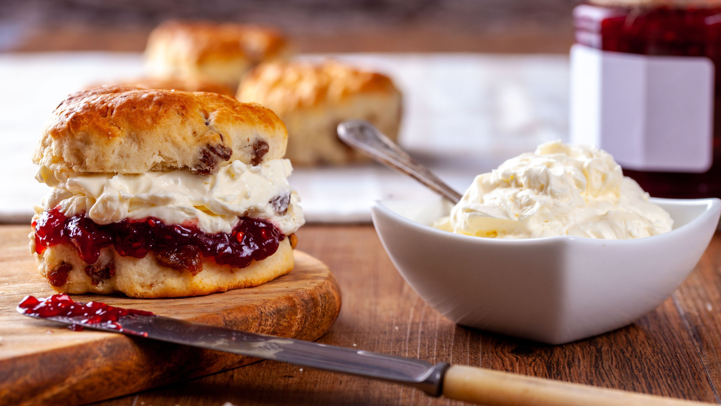 A scone filled with clotted cream and jam and a small bowl of clotted cream. 