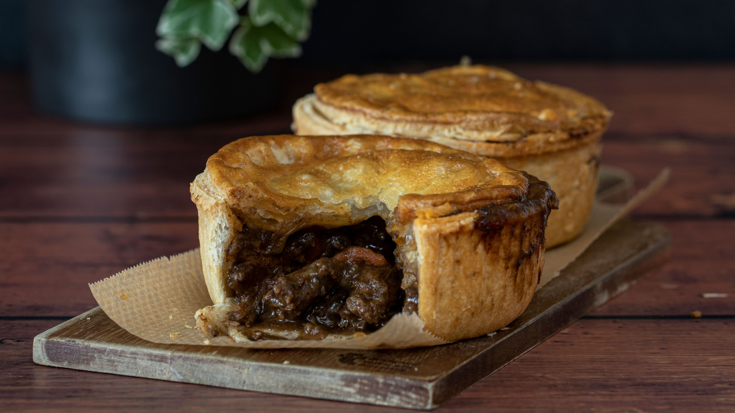 A close-up of two meat pies on a wooden board. 