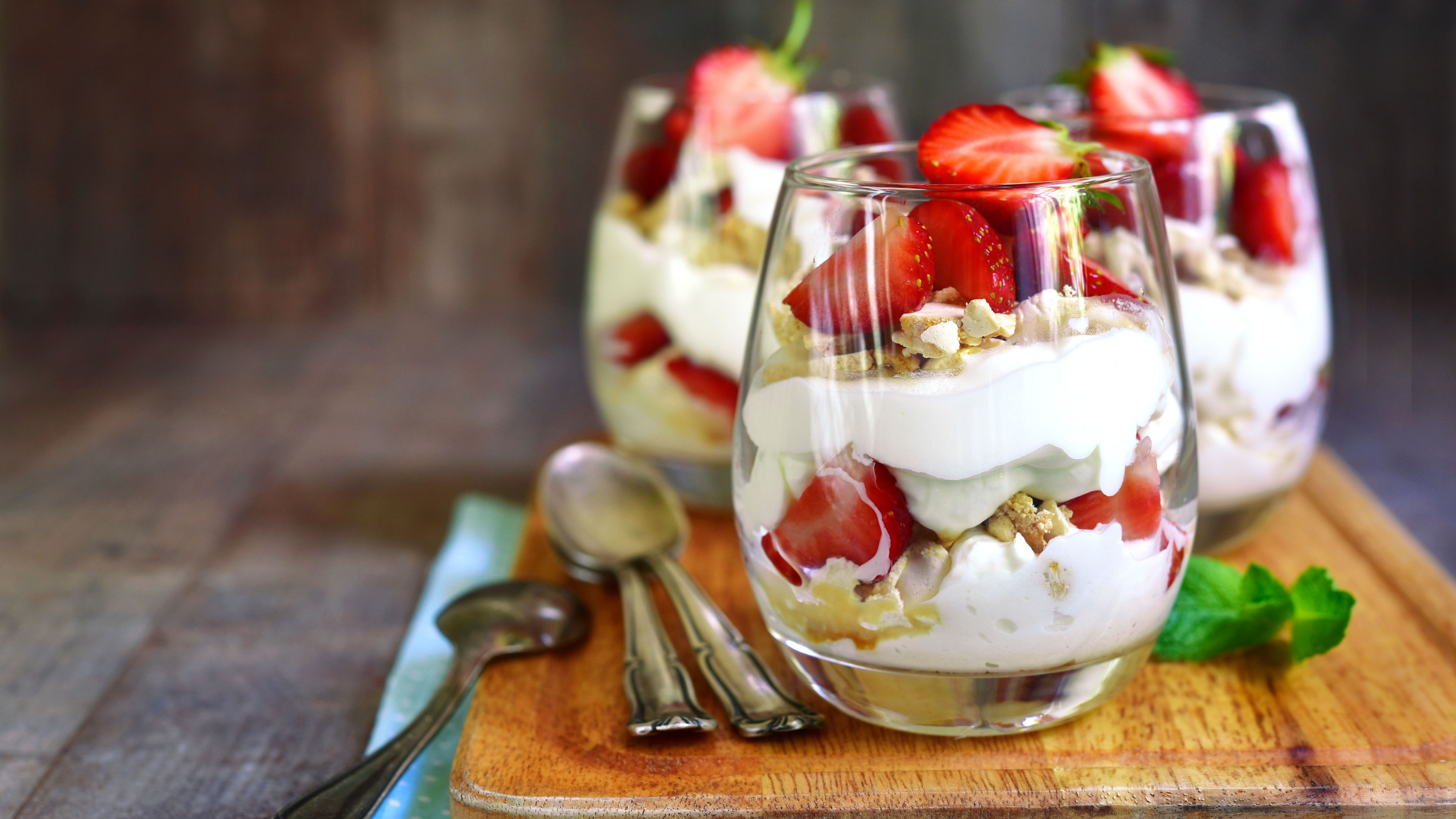 Three glasses filled with Eton Mess on a wooden board. 