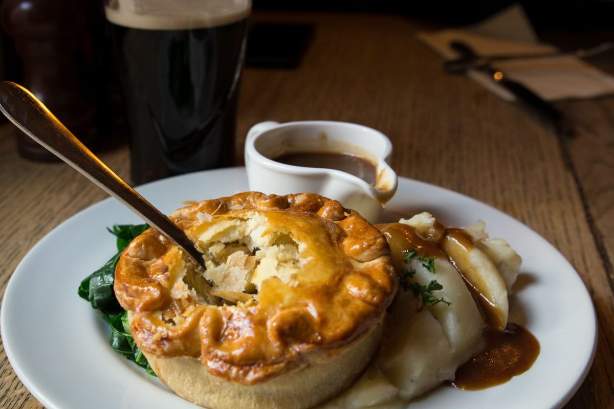 A close-up of a meat pie with a glass of beer in the background.