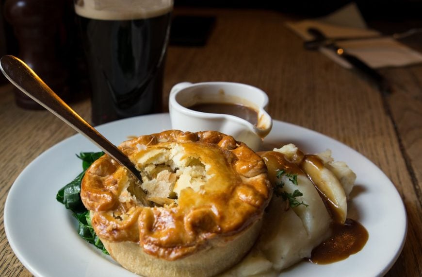 A close-up of a meat pie with a glass of beer in the background.
